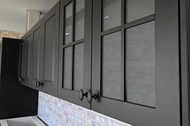 Black kitchen cabinets with black handles over a brick wall.