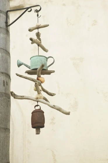 Photo of a hanging mobile made of driftwood, an old watering can, and a cow bell